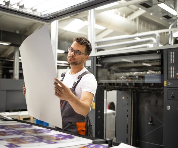 Print shop worker checking quality of imprint and controlling printing process. Print shop worker checking quality of imprint and controlling printing process.